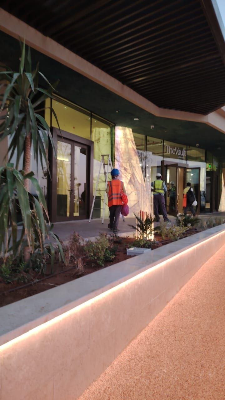 A high-end storefront (“The Vault”) during construction. Warm LED strip embedded along the planter edge, contractors visible inside in hi-vis vests.